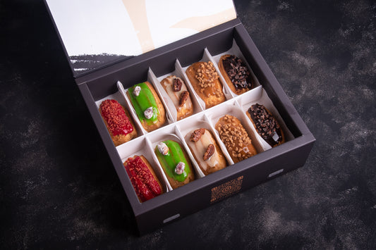 A box of assorted mini eclairs in various flavors, neatly arranged and baked with different toppings and fillings, such as chocolate chips and fruits.