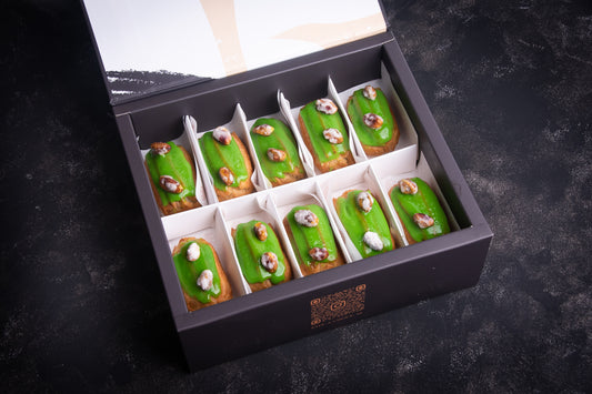 A box of assorted pistachio-flavored eclairs, with each piece topped with crystalized sugar. The eclairs are green in color, and the box is open, displaying the individual pastries.