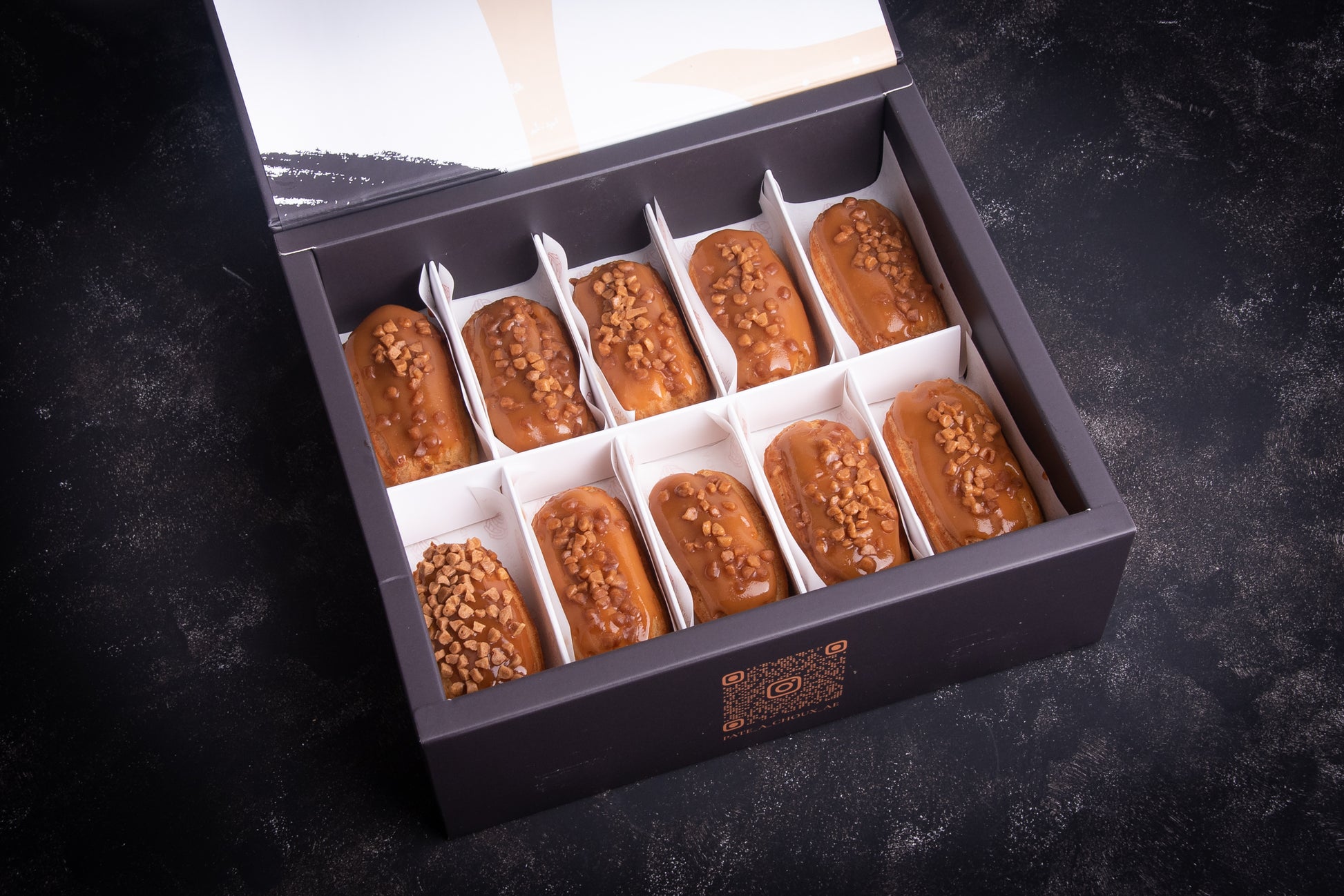 A box of salted caramel mini eclairs, with each piece individually wrapped in white paper and placed in a black box.