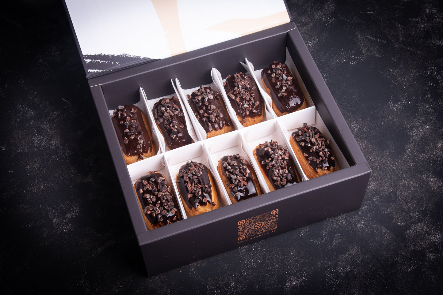 A box of Espresso Mini Éclair with individual servings of chocolate eclair, neatly arranged and presented in a dark setting.