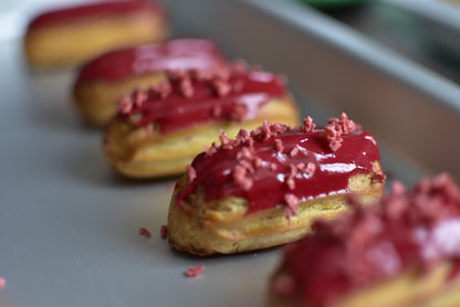 A box of strawberry mini eclairs with glazed strawberry on top, arranged in a decorative box.