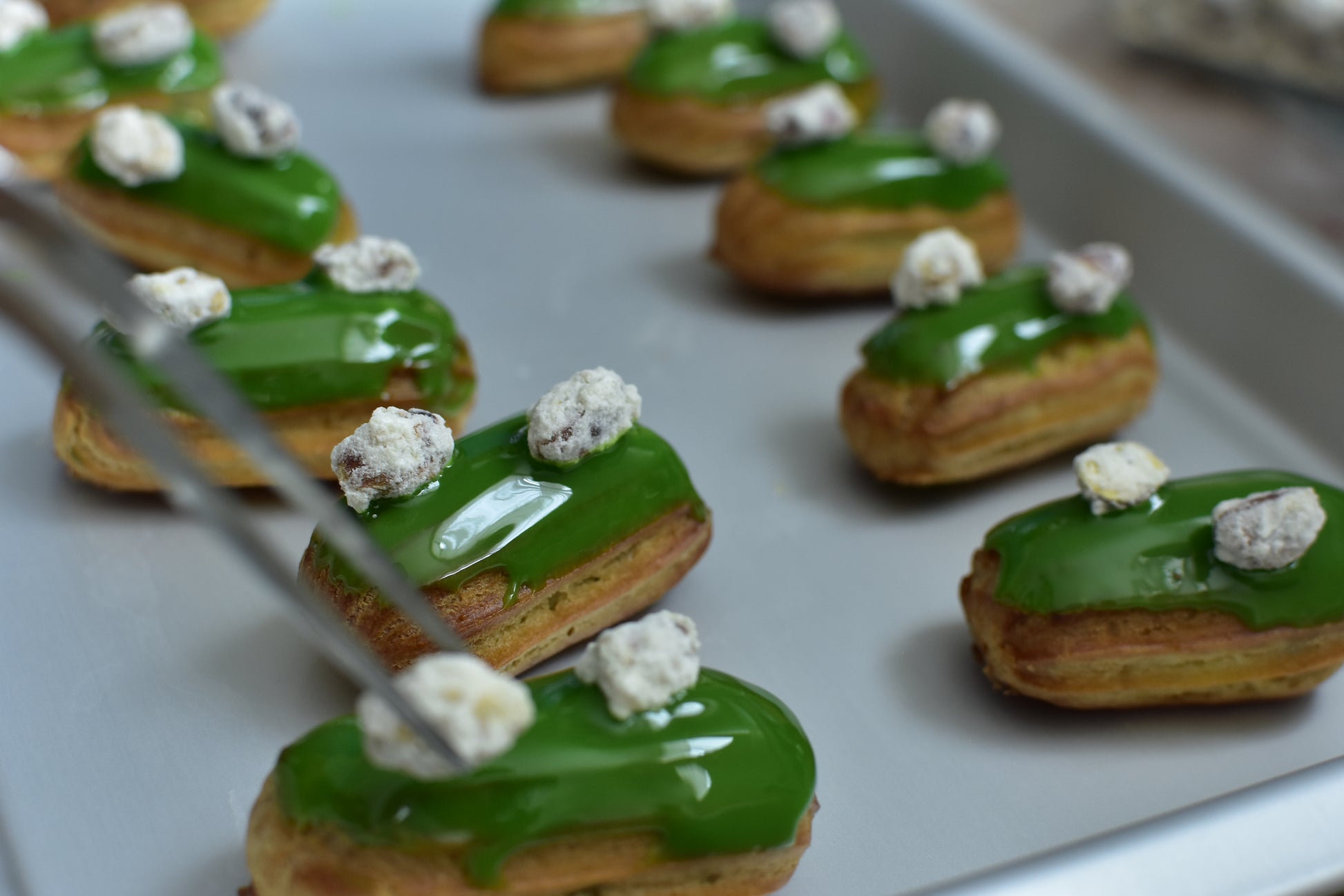 A box of pistachio mini eclairs with glazed pistachios on top, arranged in a decorative box.