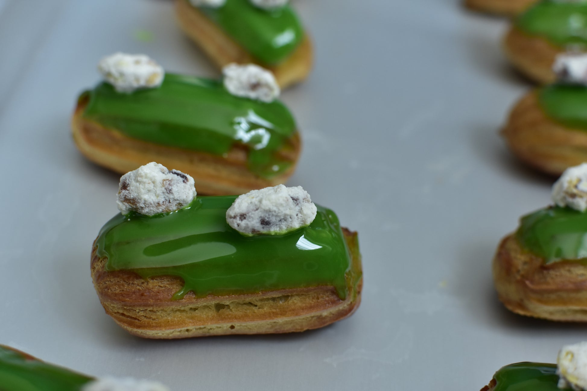 A box of pistachio mini eclairs with glazed pistachios on top, arranged in a decorative box.