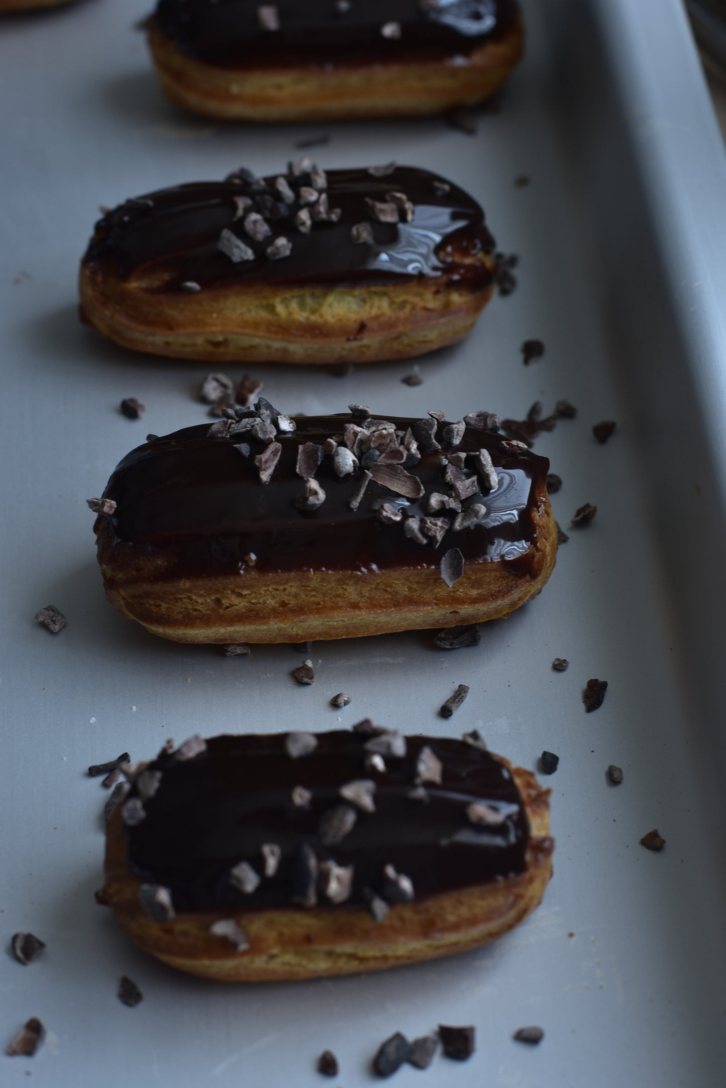A box of espresso mini eclairs with glazed chocolate chips on top, arranged in a decorative box.