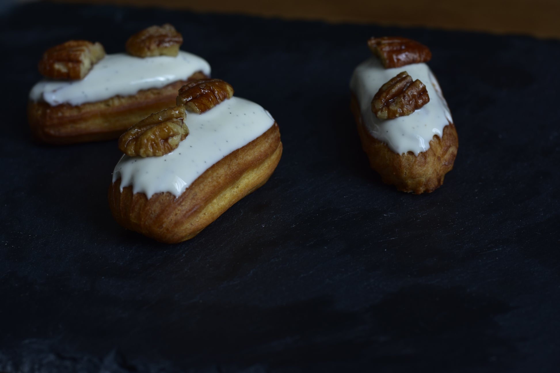 Vanilla mini eclairs with glazed vanilla on top, arranged on a decorative black surface.