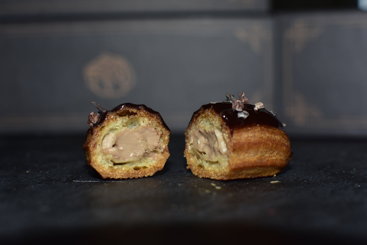 A single espresso mini eclairs cut in half showing a creamy filling with glazed chocolate chips on top, arranged on a black surface.