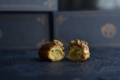 A single salted caramel mini eclair cut in half showing a creamy filling with glazed caramel on top, arranged on a black surface.